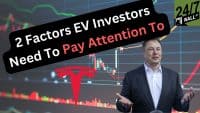 Elon Musk in a dark suit with an open-collared white shirt, gesturing with open hands, stands in front of a digital screen displaying a financial stock chart with green and red lines and bars. A large, stylized red Tesla logo is visible on the left side of the chart. A black, irregularly shaped text bubble with rounded corners angles across the top half of the image, containing the white text '2 Factors EV Investors' and 'Need To Pay Attention To' in red. In the upper right corner, a '24/7 WALL ST' logo on a green background is present.