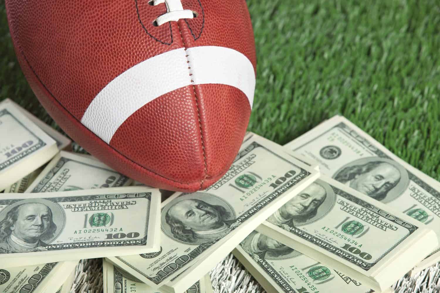 A college-style football sits with a lot of money on a green field