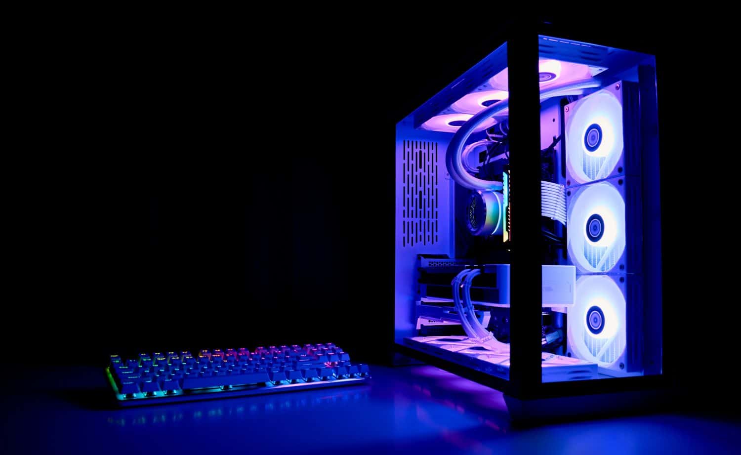 Water cooled gaming PC with rainbow RGB LED lighting. Modern gaming computer with a keyboard in a dark room. Liquid water cooling computer