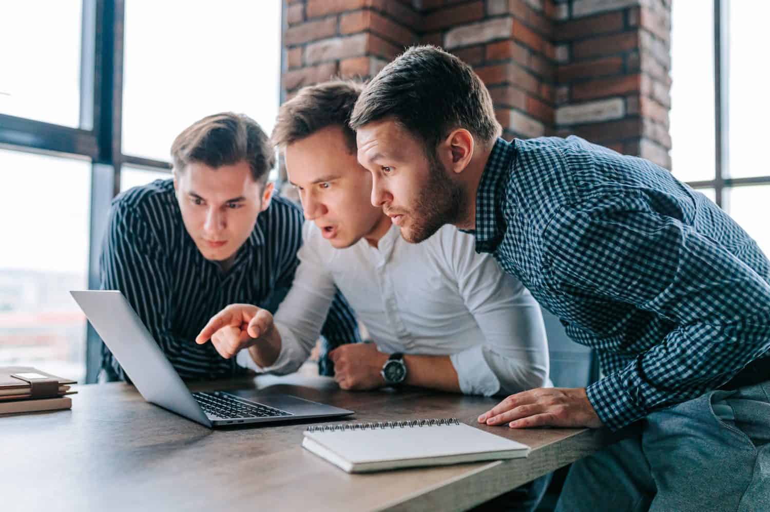 Three young men in an office, staring in amazement at their laptop screens. The work before them seems to have left them stunned and stunned.