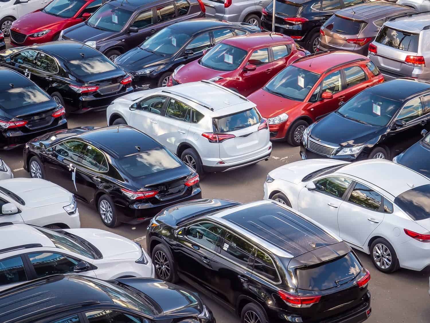 Selling new and used cars in a dealership. Lots of cars in the parking lot. Black, white, silver and red cars of unknown brands