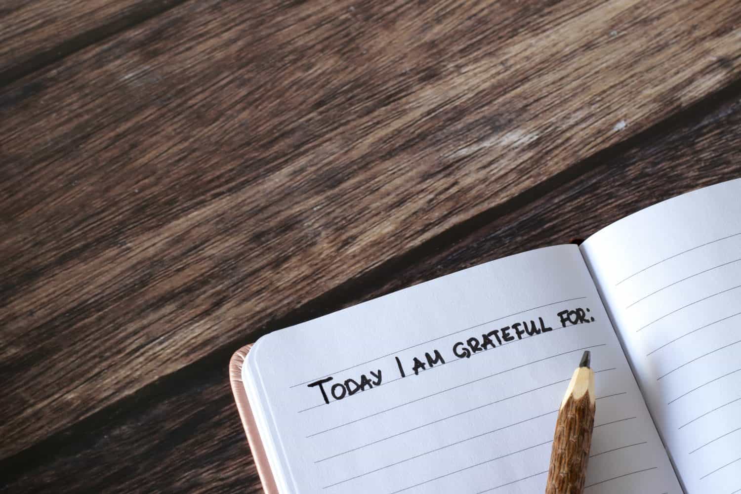 Open diary with handwritten text for gratitude and thanks and pencil on wooden table. Top view, copy space. Thanking God Jesus Christ for the blessings in the personal notebook.