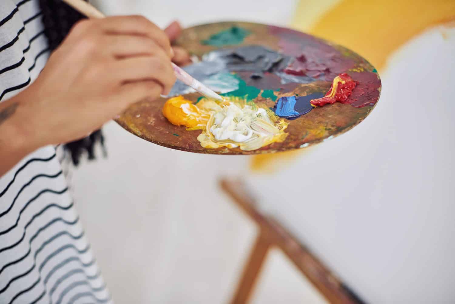 Person, hands and art with palette in closeup for painting on canvas for hobby and creative vision at home. Painter, artwork and oil color mixing with brush in workshop for inspiration and expression