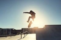 Skateboard, man and jumping in urban skate park with trick and training in Los Angeles with speed. Sunshine, deck and skater in the city with balance, skating competition and fun board flip by ramp