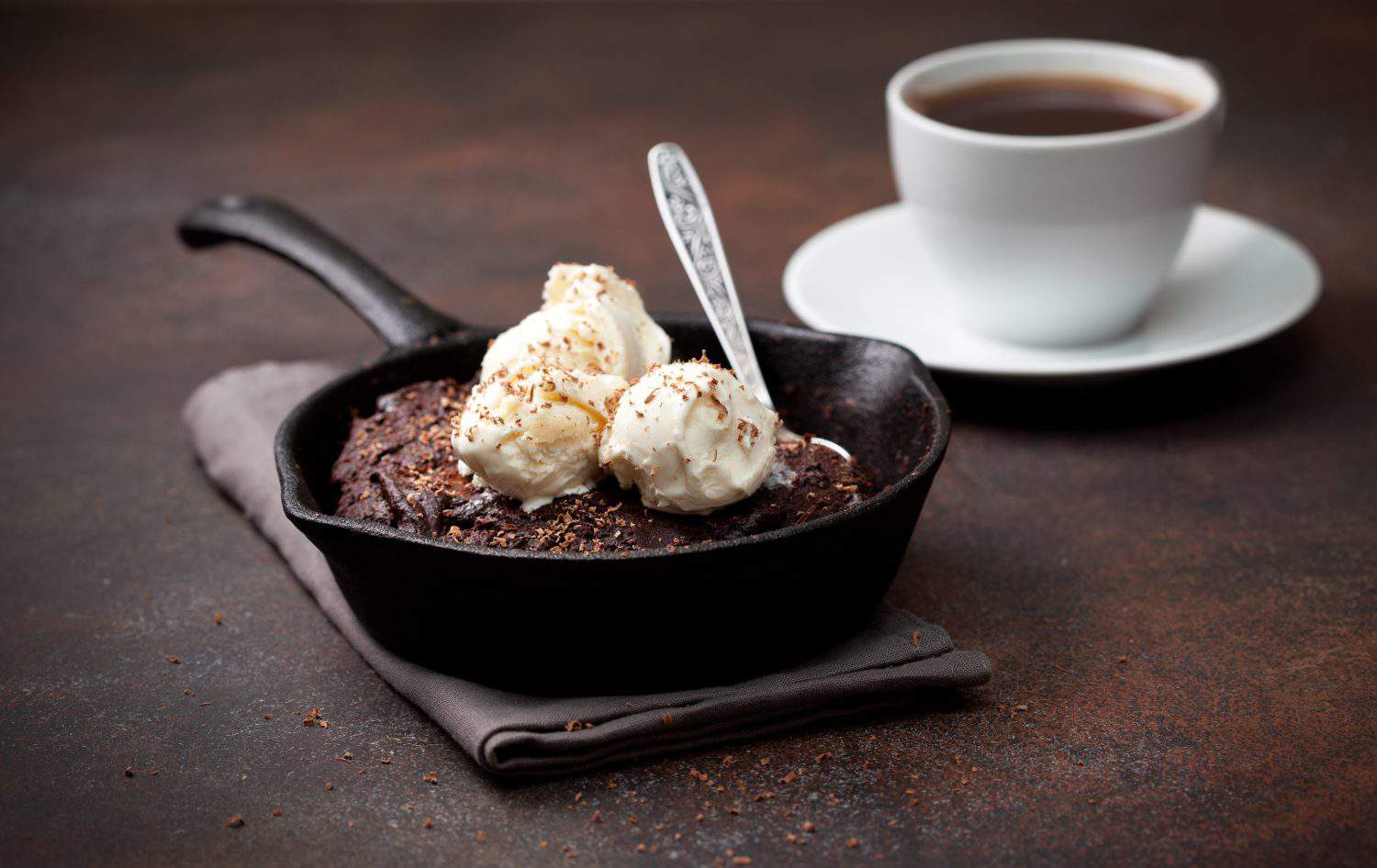 brownie with vanilla ice cream in a pan, a cup of coffee on a brown background