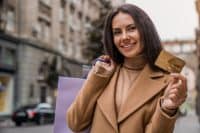 Young caucasian woman female with shopping bags and credit card enjoying shopping standing outdoors at the city street. Black friday concept. E-banking