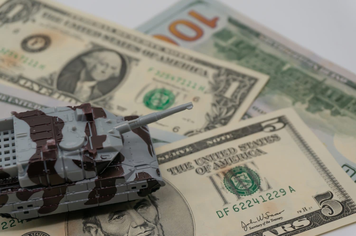 The tanks are placed on top of the bills. A metaphor for currency wars, financial crises, trade wars, tariff sanctions, international competition, the costs of war and military spending.