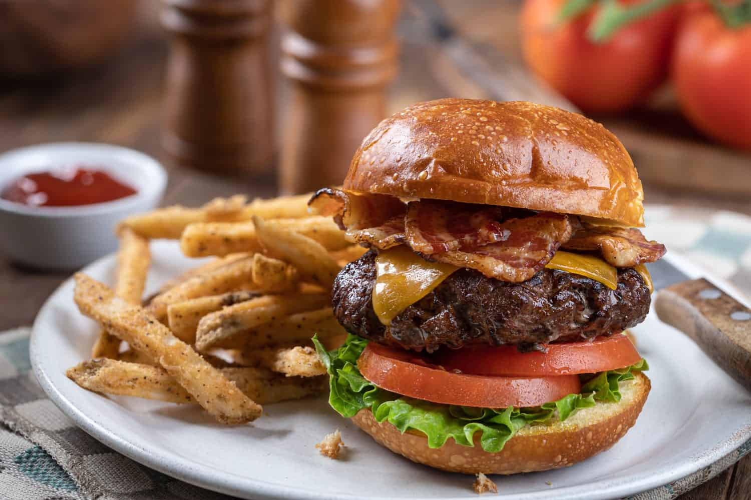 Bacon cheeseburger with lettuce and tomato on a toasted bun and fries on a plate