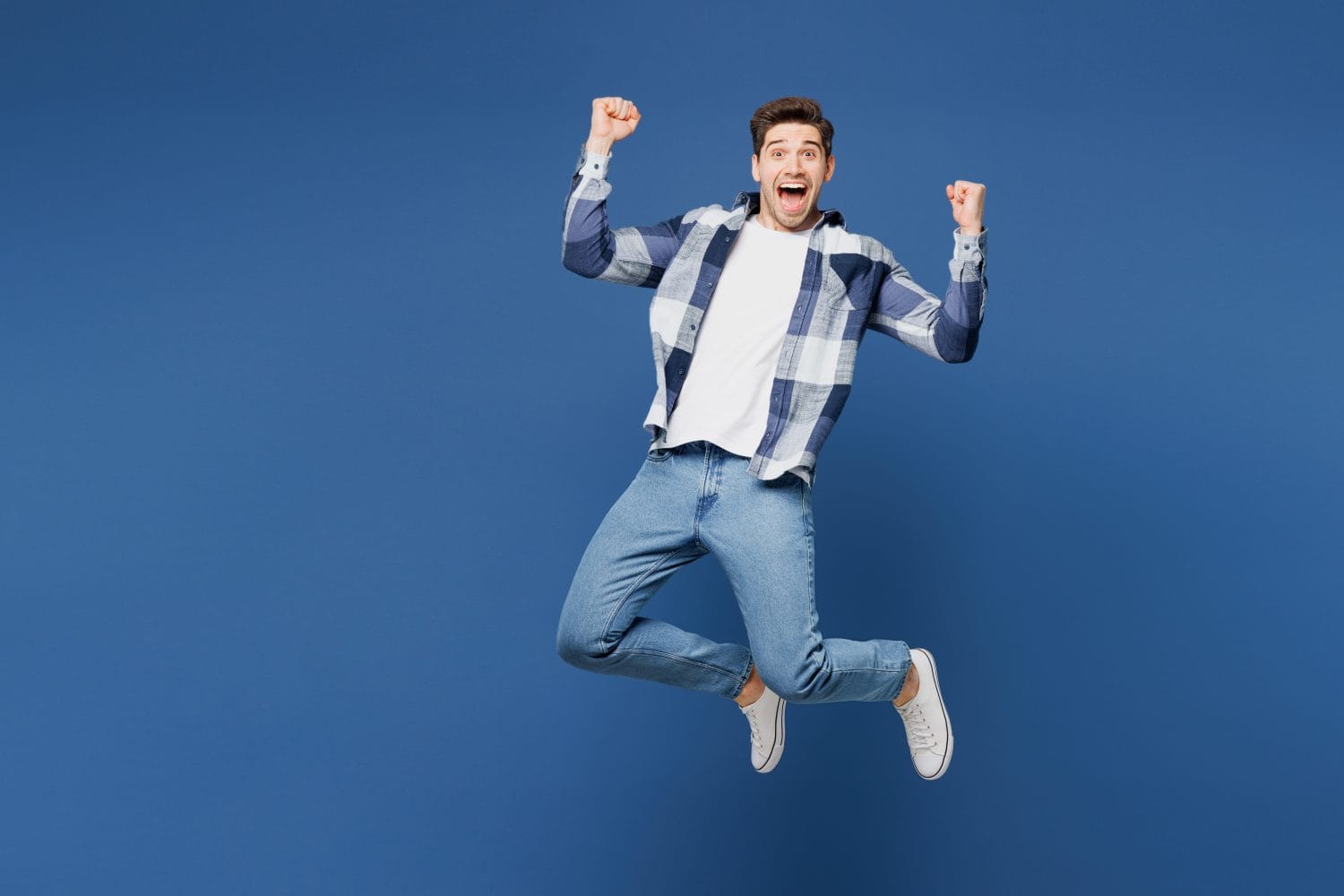 Full body young happy man he wears shirt white t-shirt casual clothes jump up making winning gesture celebrate clenched fists isolated on cyan blue background studio portrait. Lifestyle concept