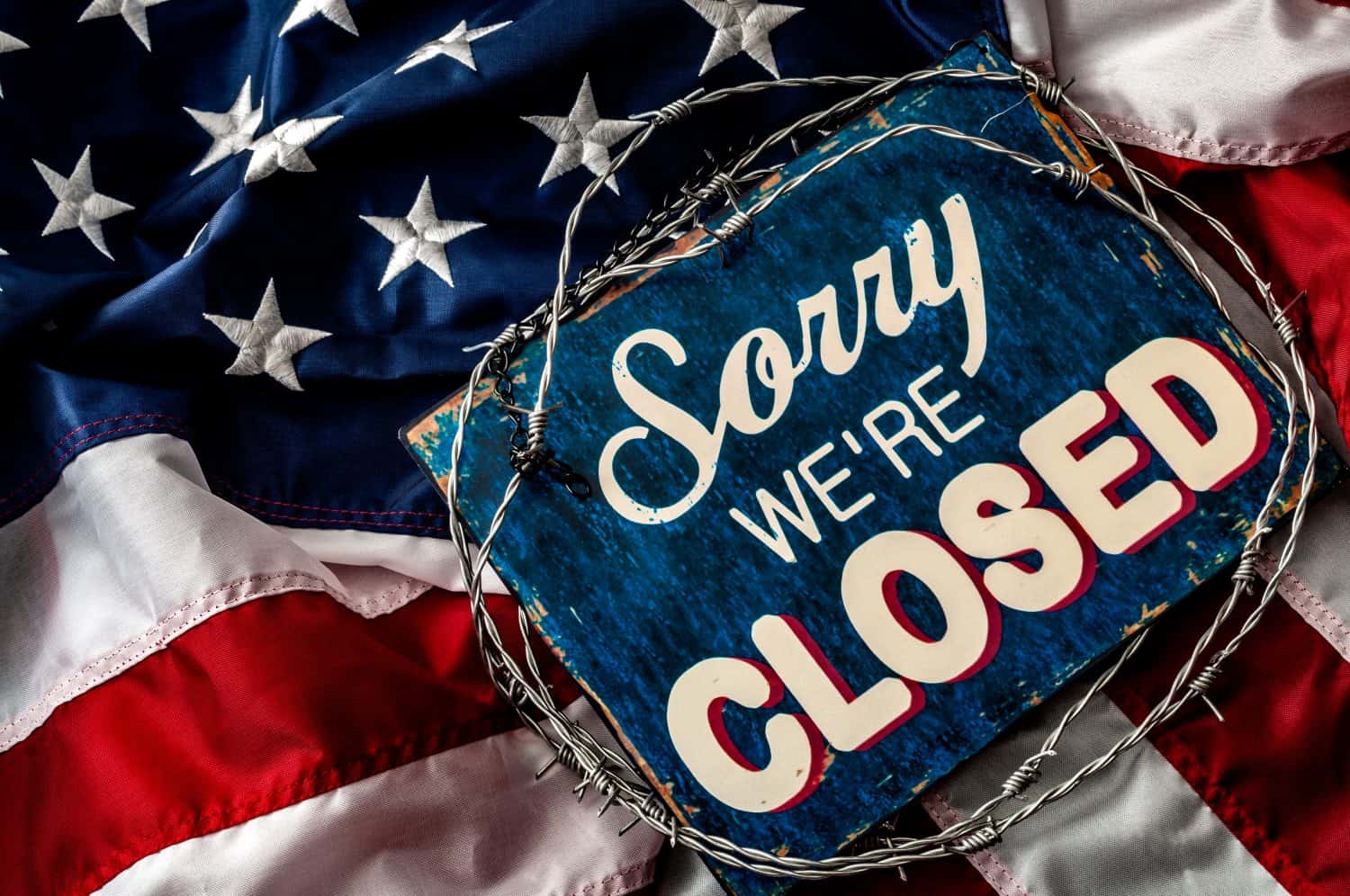 Political isolationism and economic slowdown in the United States of America concept with close up a sorry we're closed sign wrapped in barbwire on top of the american flag