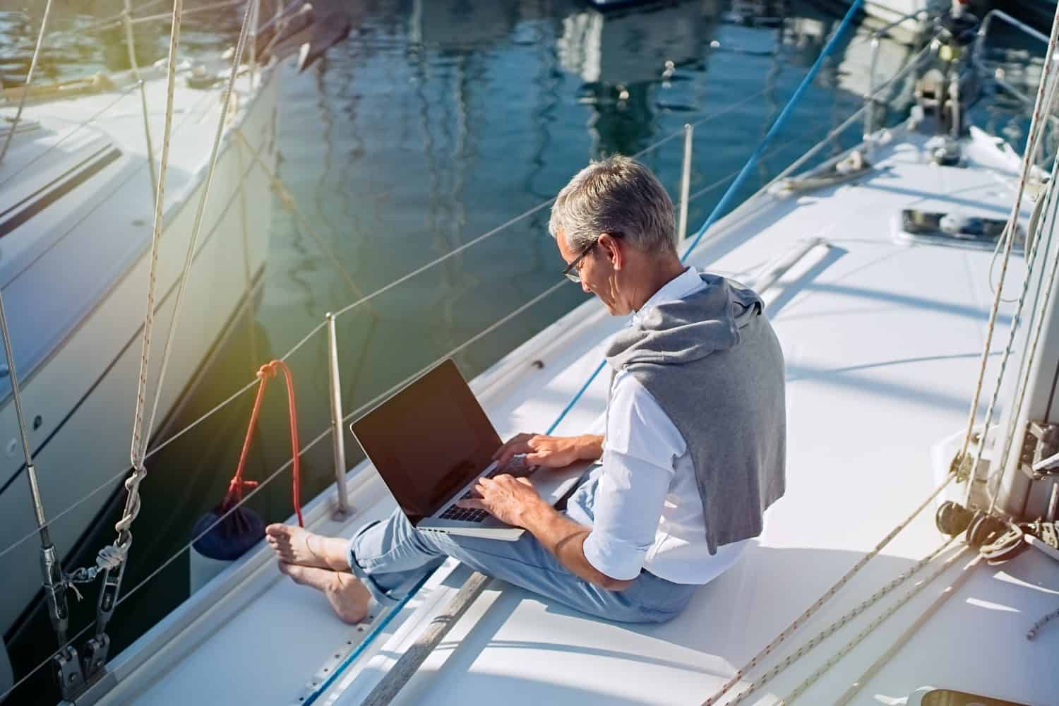 Senior businessman is working during the vacation on a sailboat