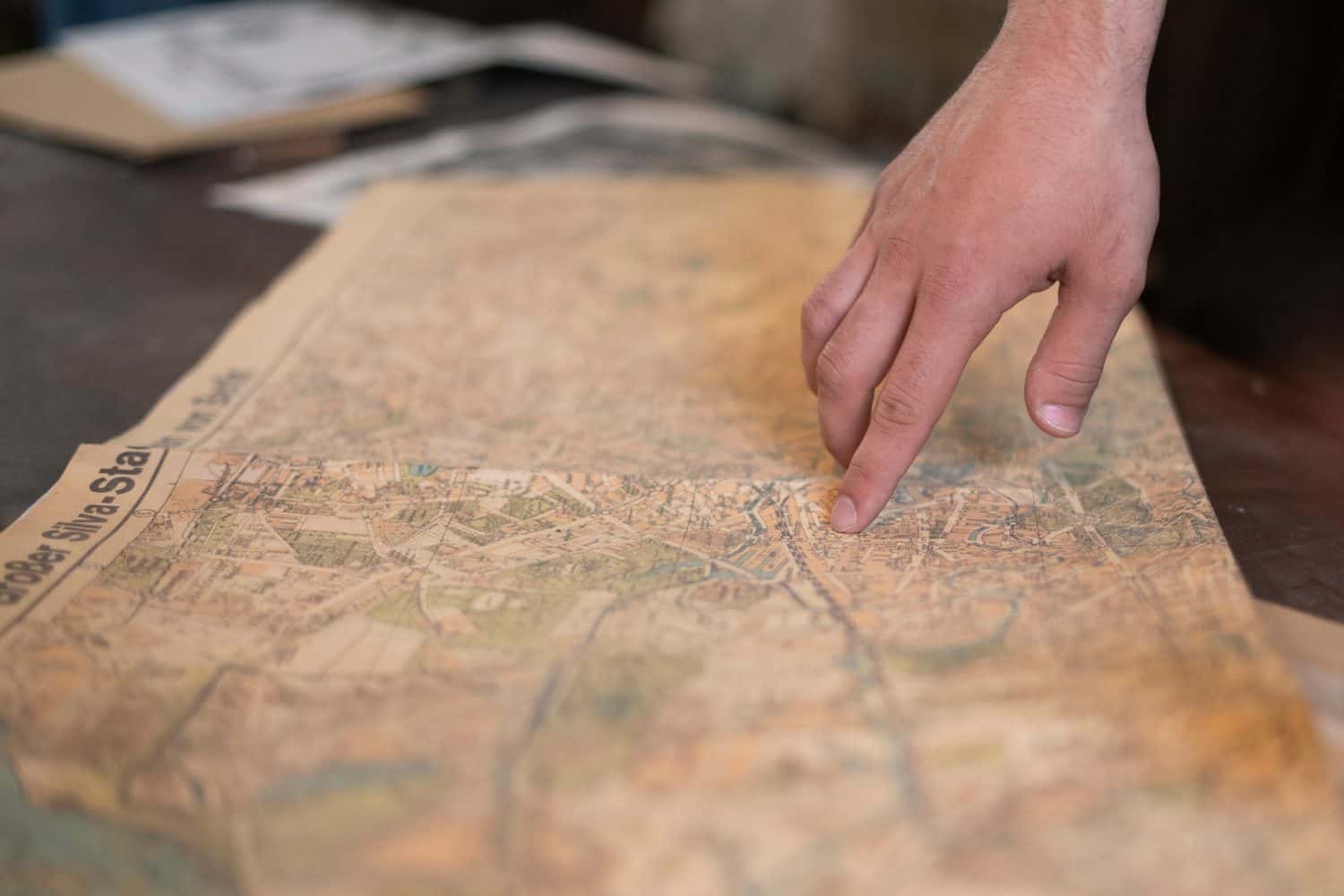 a person's finger pointing on the old map to go to the destination