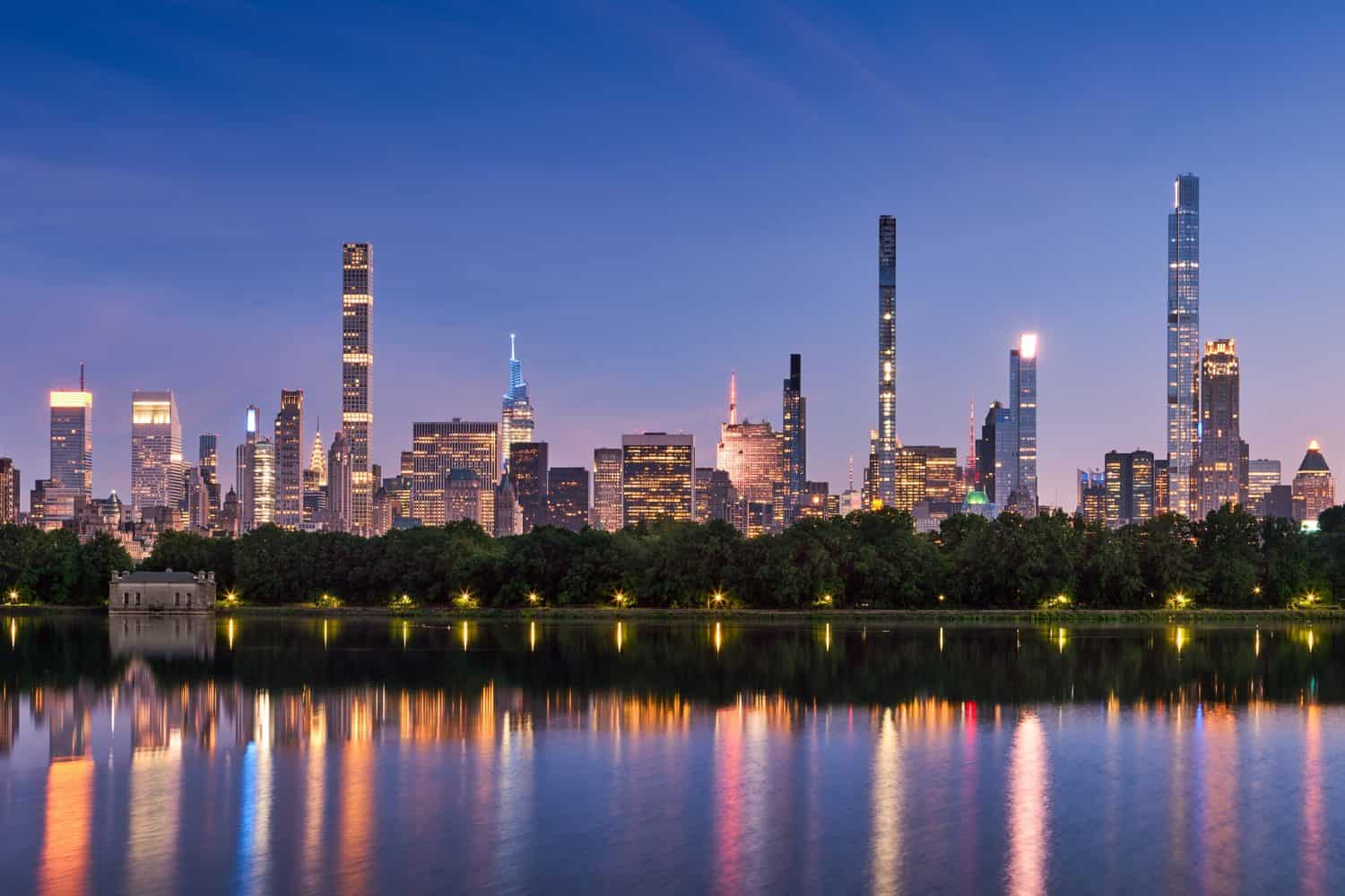 New York City skyline at dusk with reflections of Billionaires Row supertall skyscrapers in Central Park Reservoir. Evening view of illuminated luxury towers in Midtown Manhattan