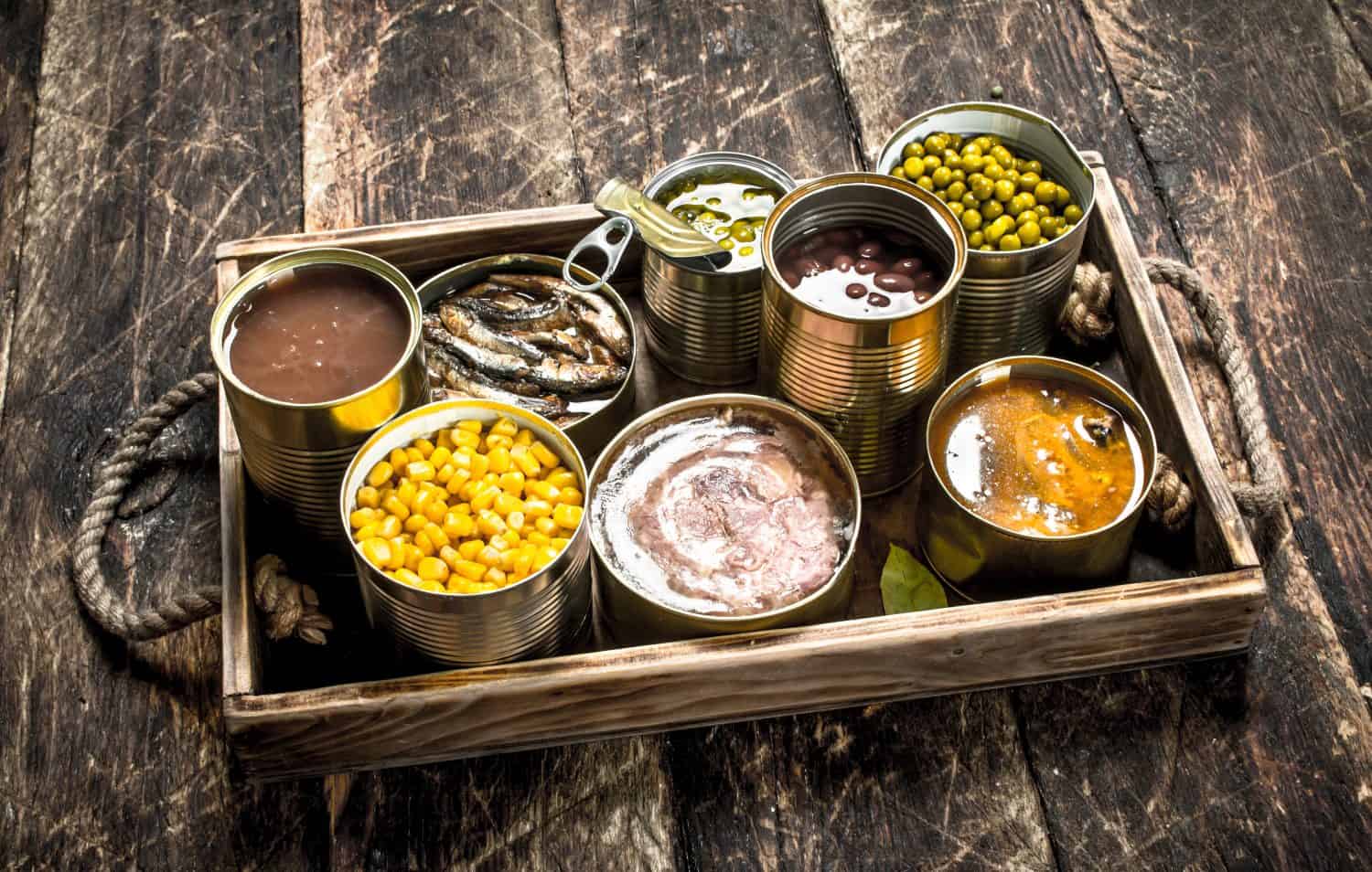 Various canned fruits, vegetables, canned fish and meat on old tray. On a wooden background