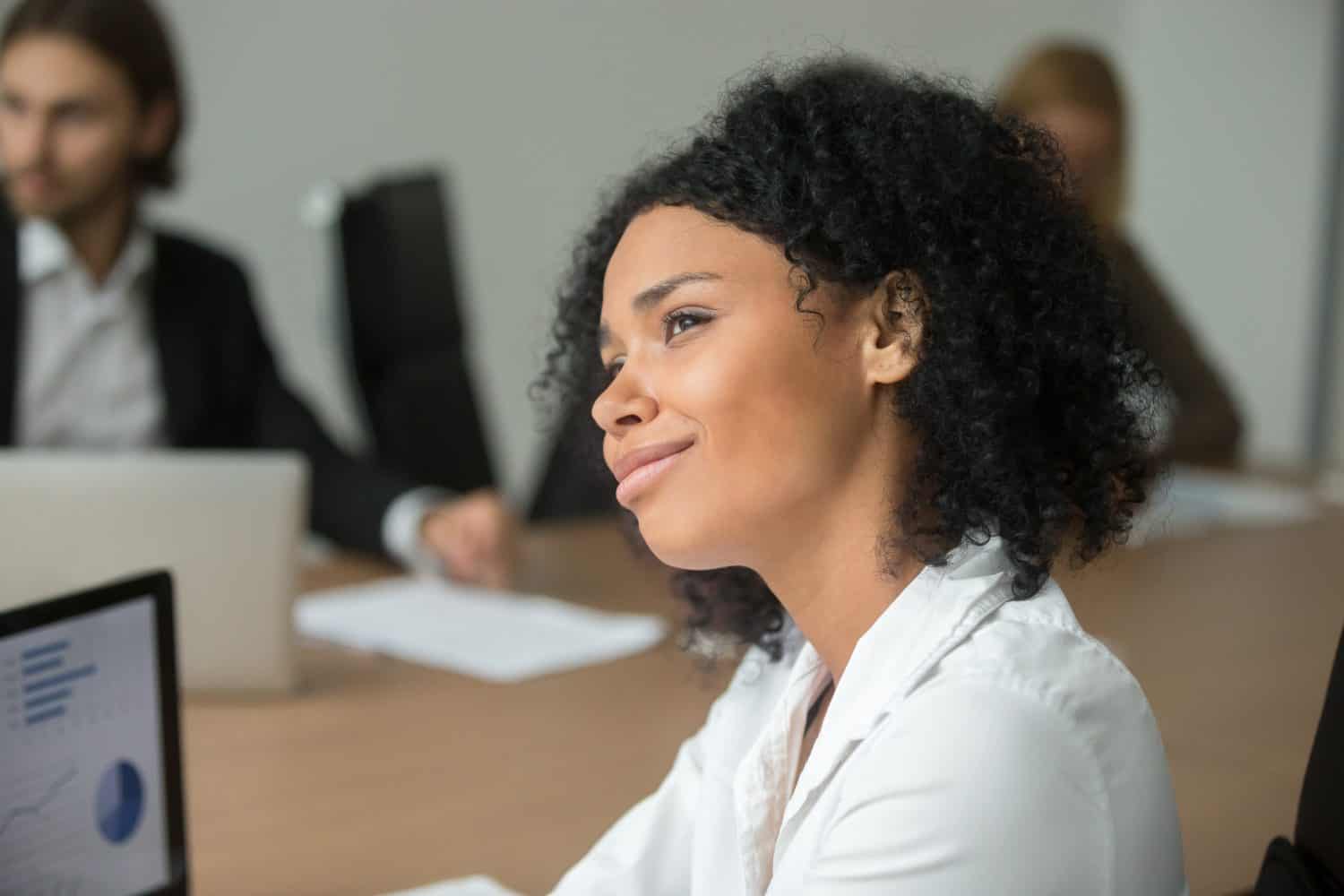 Smiling african american businesswoman looking to future thinking of business success at meeting, dreamy absent-minded black employee dreaming of vacation or making career plans, head shot portrait