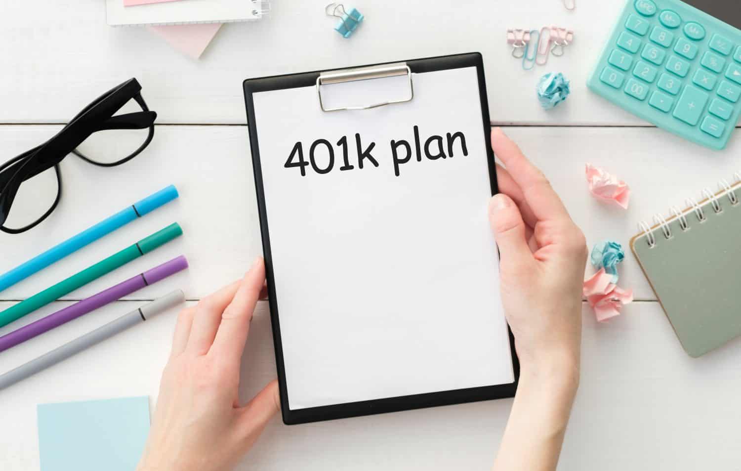 Businessman holding a card with text 401K. PLAN Keyboard, diagram and wooden background