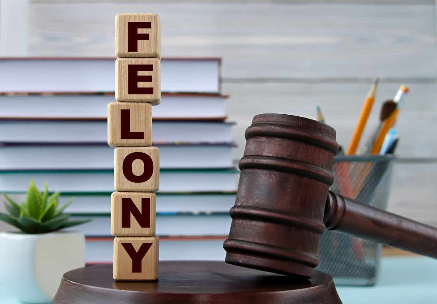 The word FELONY on wooden cubes against the background of the judge's gavel and stand. Business concept