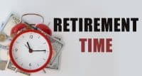 A red alarm clock is placed on a light gray surface, surrounded by scattered US dollar bills and coins. The clock face is white with black numbers, and its hands indicate approximately 10:15. To the right of the clock, bold black text reads 'RETIREMENT' above bold red text that says 'TIME'.