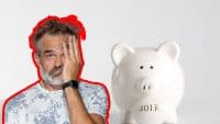 A man with a grey beard and hair, wearing a patterned shirt and a smartwatch, covers part of his face with his hand, looking stressed. To his right is a white piggy bank with '401 K' written in gold on its side. The background is white.