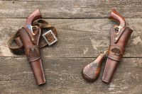Black powder revolvers in a leather holster with a leather belt and gunpowder flask on the background of old, worn boards.