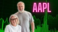 A smiling older man with a gray beard and a smiling older woman with gray hair and black-framed glasses are positioned in the foreground. Behind them is a digital stock market graph with green lines and vertical bars indicating an upward trend on a dark green grid. The ticker symbol 'AAPL' is prominently displayed in large pink letters at the top right of the graph.