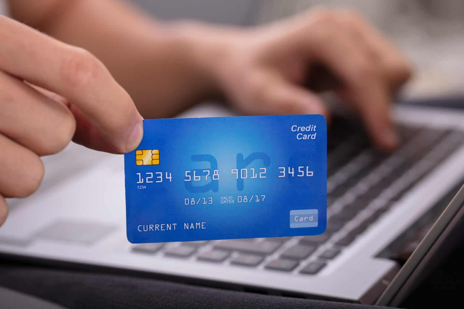 Close-up Of A Man's Hand Holding Credit Card While Shopping Online On Laptop