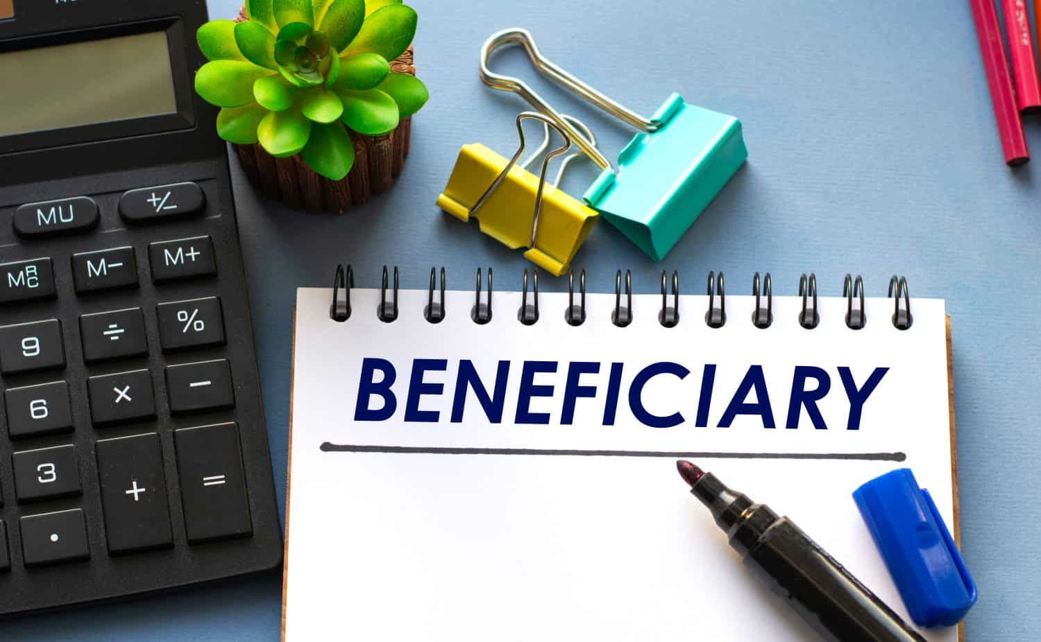 BENEFICIARY word is written in a notebook with a marker, calculator, clamps and cactus. Business concept