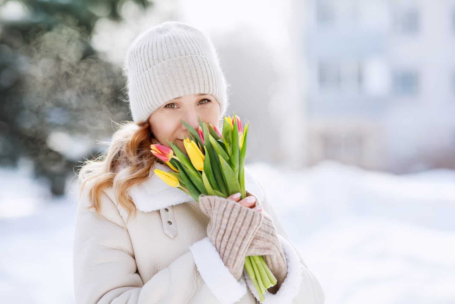 A girl with a bouquet of yellow and pink tulips on a walk on a sunny winter day. Flowers for International Women's Day. The nature of Siberia in Russia.