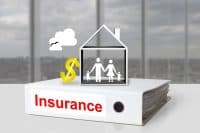 A white binder labeled 'Insurance' in red text sits on a white table. Above it, a white outline of a house contains stick figures of a family: two adults and two children. To the left of the house is a shiny golden dollar sign, and above it, a white cloud with two black bird silhouettes. The background shows a blurred view through large office windows.