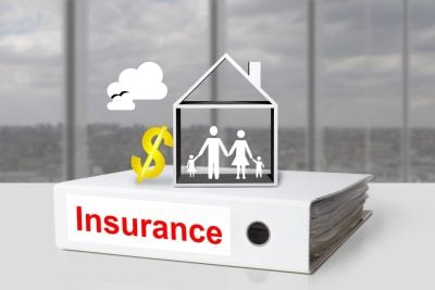 A white binder labeled 'Insurance' in red text sits on a white table. Above it, a white outline of a house contains stick figures of a family: two adults and two children. To the left of the house is a shiny golden dollar sign, and above it, a white cloud with two black bird silhouettes. The background shows a blurred view through large office windows.