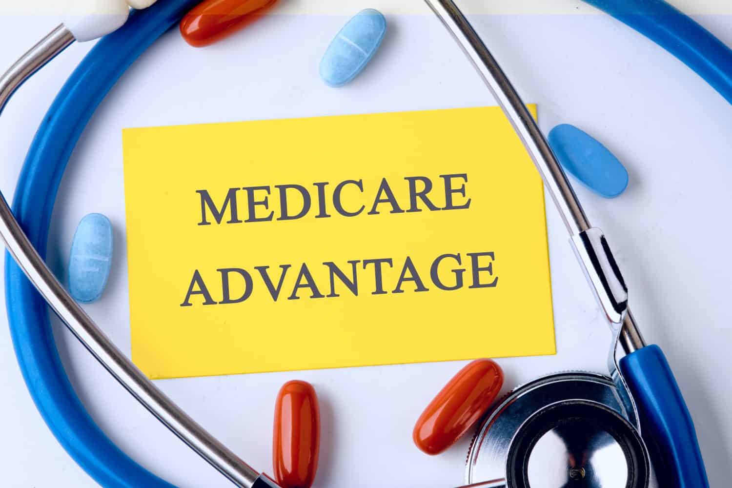 Medical and health concept. Phrase MEDICARE ADVANTAGE written on a yellow business card in a composition with a stethoscope and pills