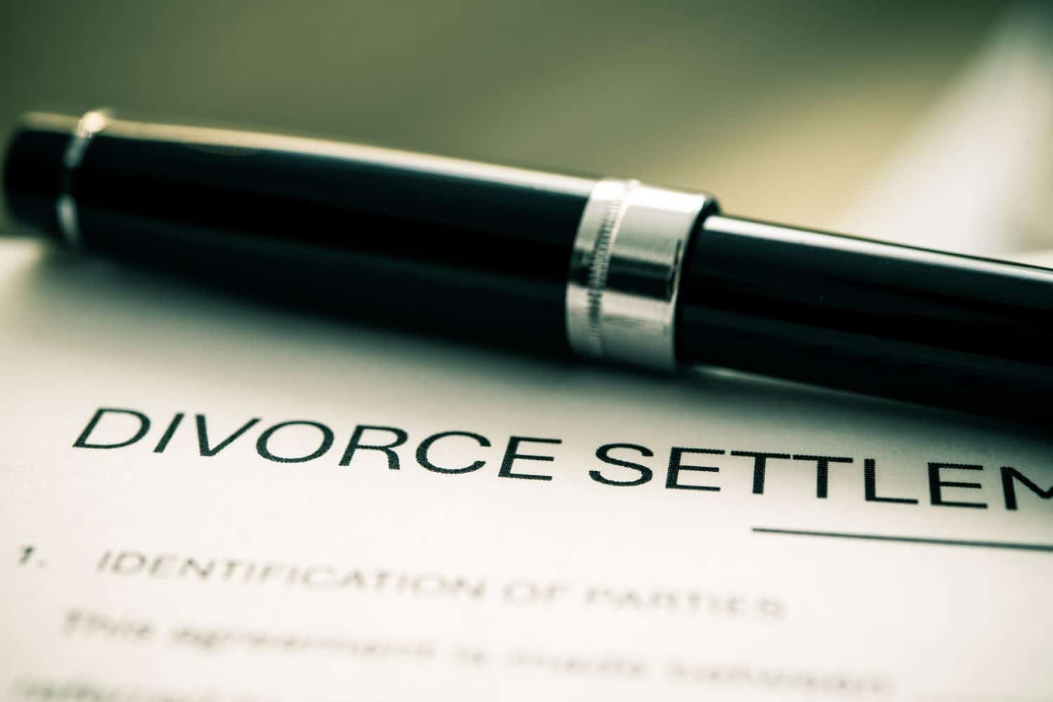 Detailed divorce settlement agreement form printed on paper, accompanied by a pen, signifies legal proceedings related to marital dissolution and negotiation between involved parties.