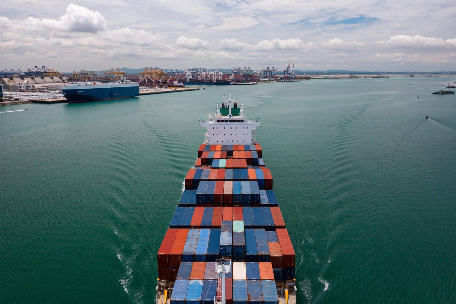 Aerial view of a large cargo ship entering a busy container port, showcasing maritime trade and logistics operations.