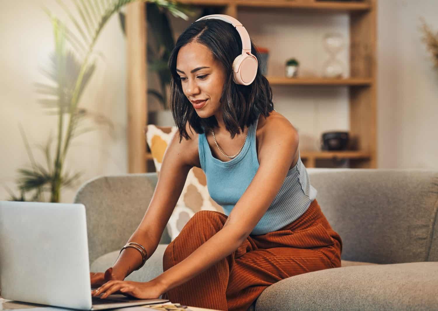 Woman, typing or headphones at laptop for remote work, editing or productivity on home sofa. Freelance transcriptionist, writer or tech in living room for audio translation, subtitle or communication