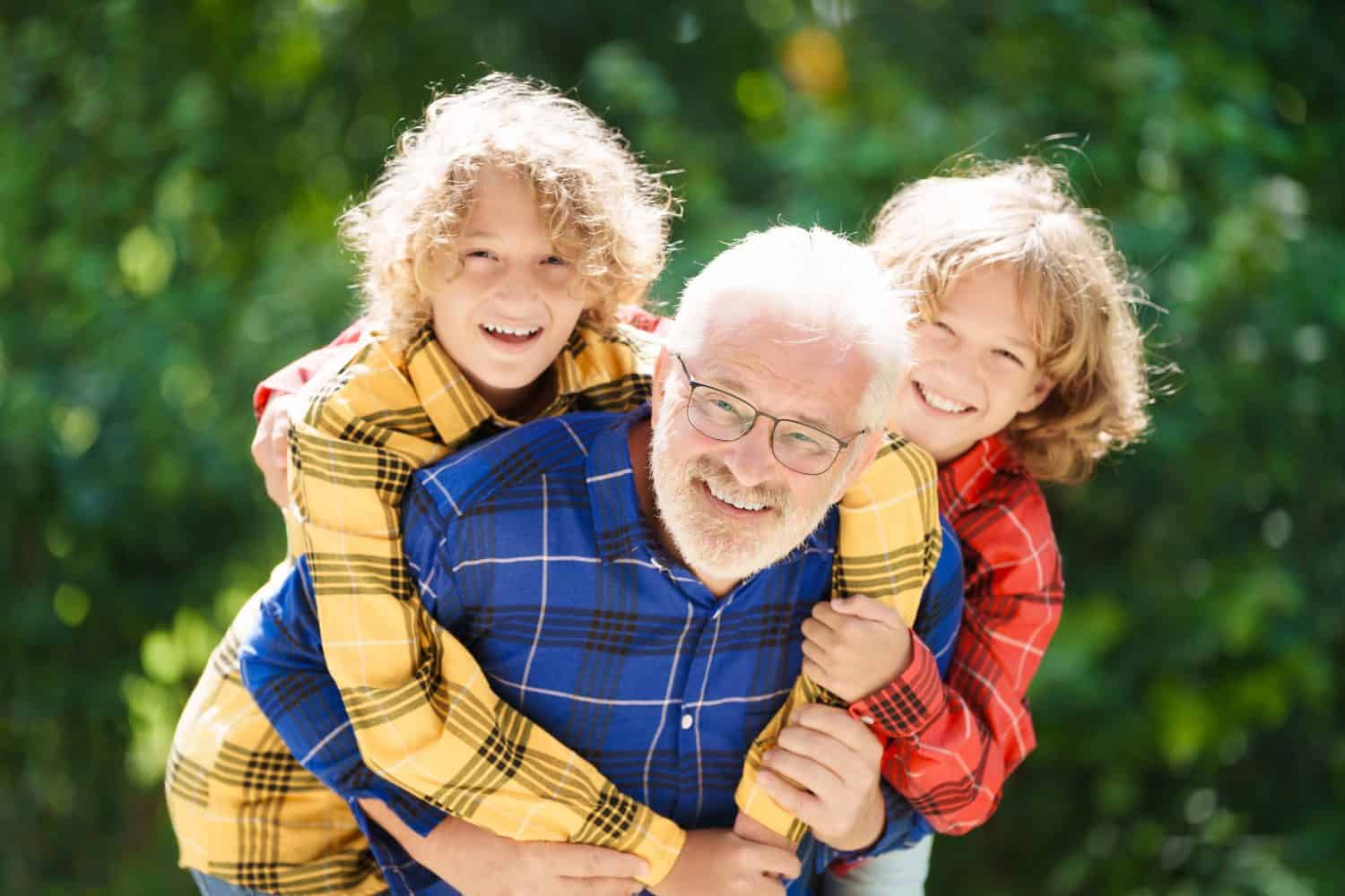 Grandfather and kids in sunny garden. Happy family playing in summer park. Grandpa and children play outdoor. Generation love. Active senior man with little boy. Grandchildren visit grandparents.