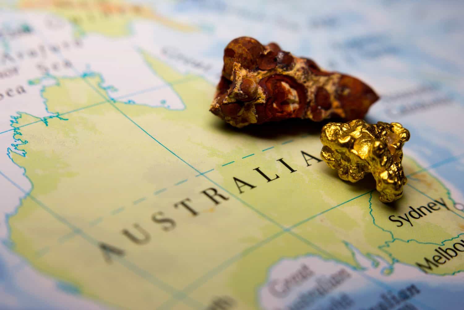 Close-up of Bauxite mineral and gold nugget on top of a map of Australia