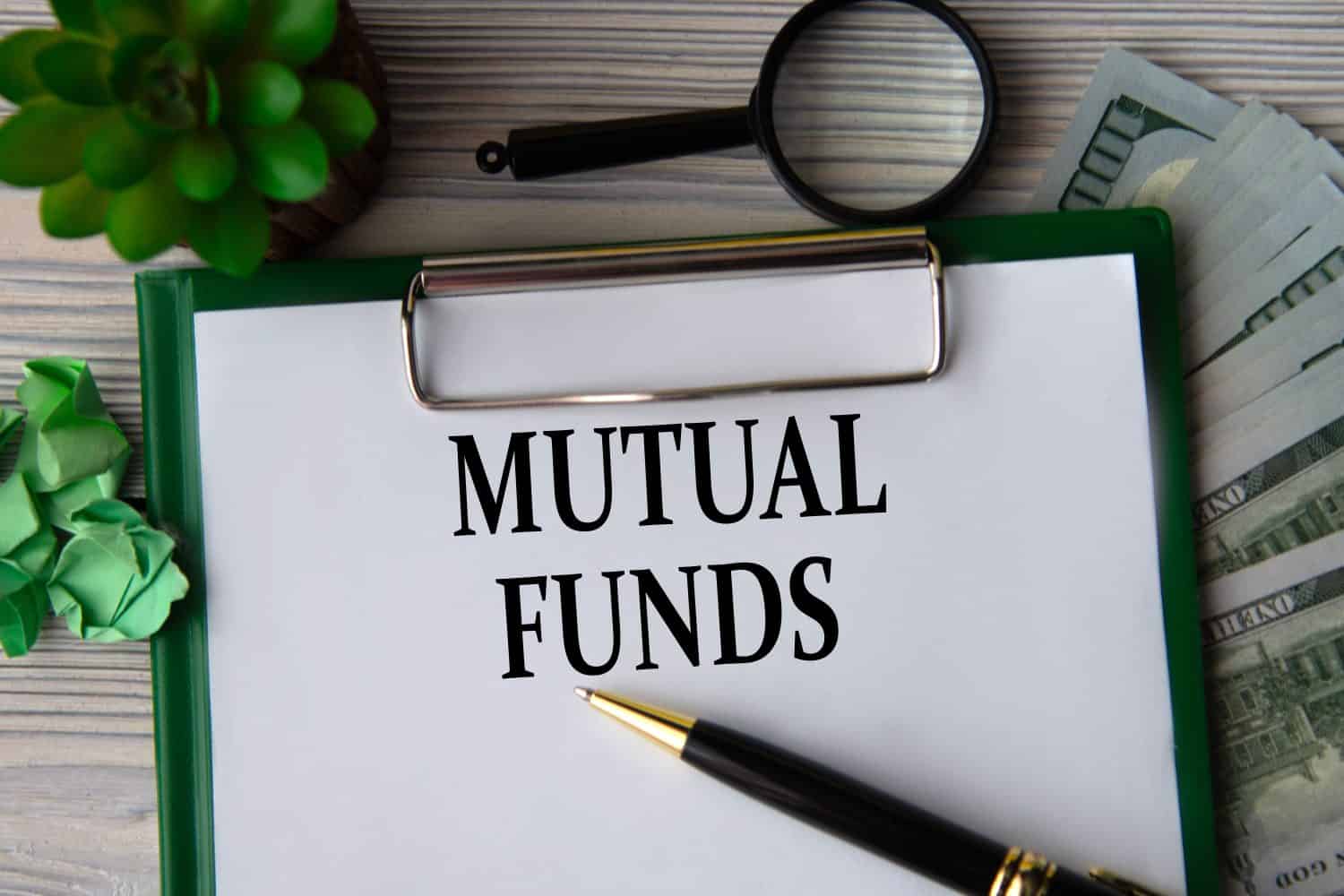 MUTUAL FUNDS - words on a white sheet against the background of banknotes, magnifying glass and cactus