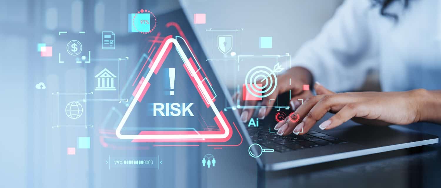 A person types on a laptop with holographic financial icons and a risk warning sign overlay. The background is blurred. The concept is risk management in a digital financial context