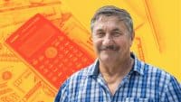 A smiling older man with a mustache and a blue and white plaid shirt looks directly at the viewer. He is positioned in front of a background with an orange and yellow filter, featuring a Casio scientific calculator and scattered U.S. dollar bills.