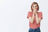 Girl trying to hide secret, wanting to tell everyone, being talkative. Excited over-emotive european female student in striped t-shirt, covering mouth with palms not to say word, shocked and intense