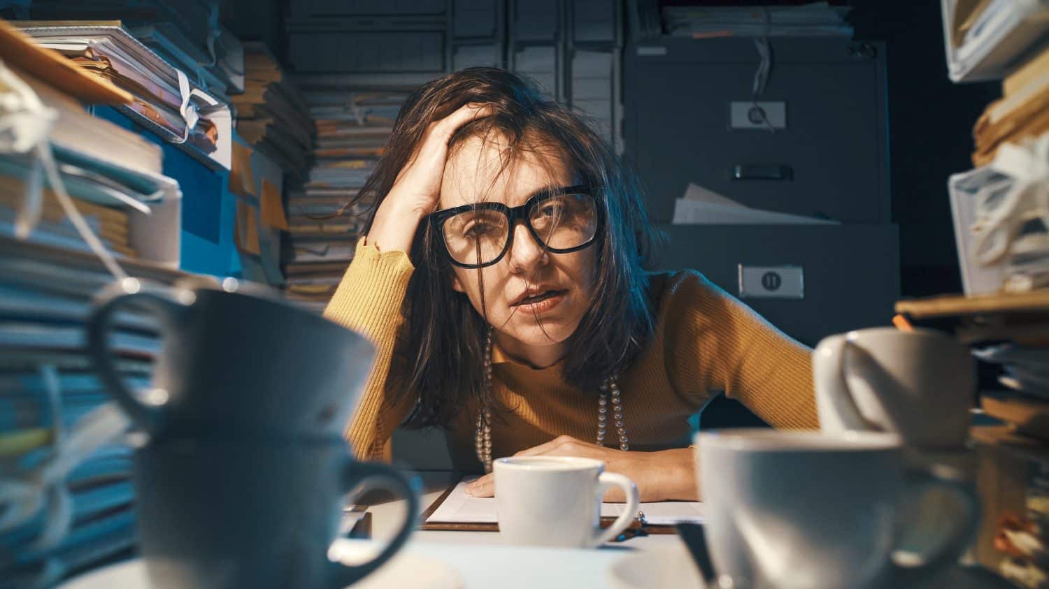 Stressed exhausted woman sitting at office desk and working overtime, she is overloaded with work