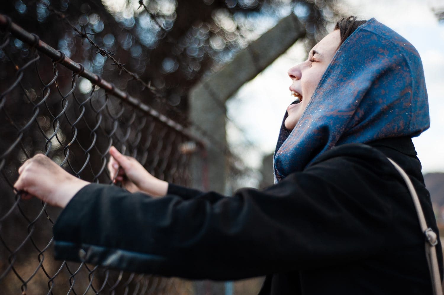 The migrant is holding his hands behind the protective fence