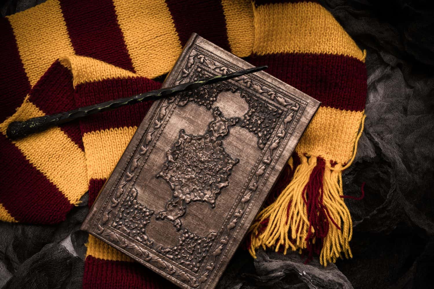 Subjects of the school of magic. Scarf, magic wand, book of spells on grey dark rag background.