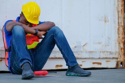 American African engineer or technician worker man sit close to cargo container and he look tired and sleepy or lost job. Concept of good system and manager support for better industrial business.