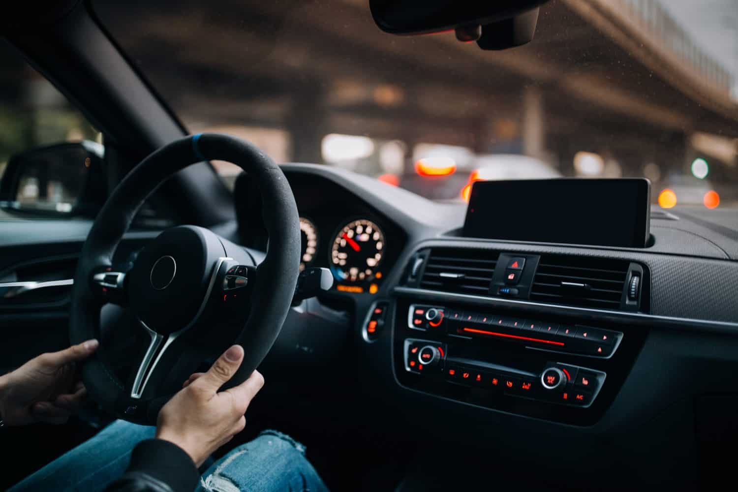 Driving a car in the city. A man driving his modern sports car in the city center. A driver stuck in traffic. Modern car interior with big multimedia screen, sport steering wheel. Driver hold steering