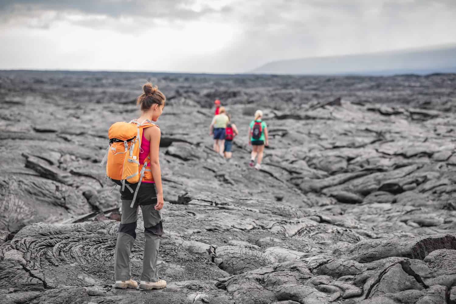 Hiking group of hikers walking on Hawaii volcano lava field hike adventure happy woman with backpack in Big Island, Hawaii. Tourists walking on guided tour trail outdoor USA summer travel vacation.