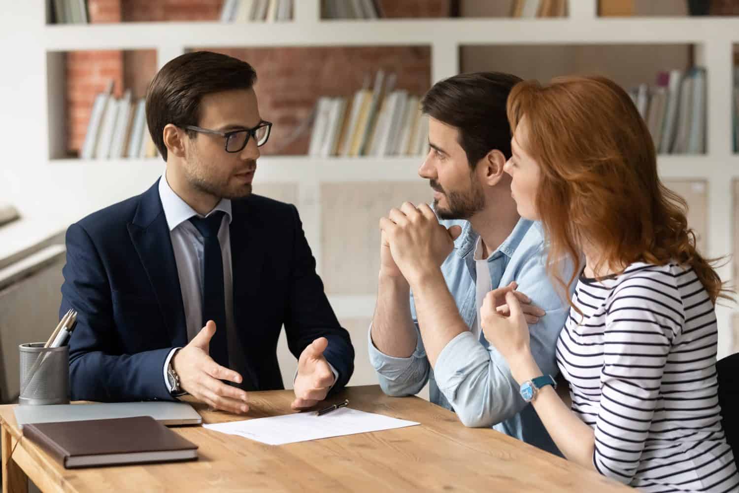 Professional male lawyer financial advisor consulting happy family couple clients in modern office. Interested young customers meeting realtor broker bank worker, discussing agreement or deal.