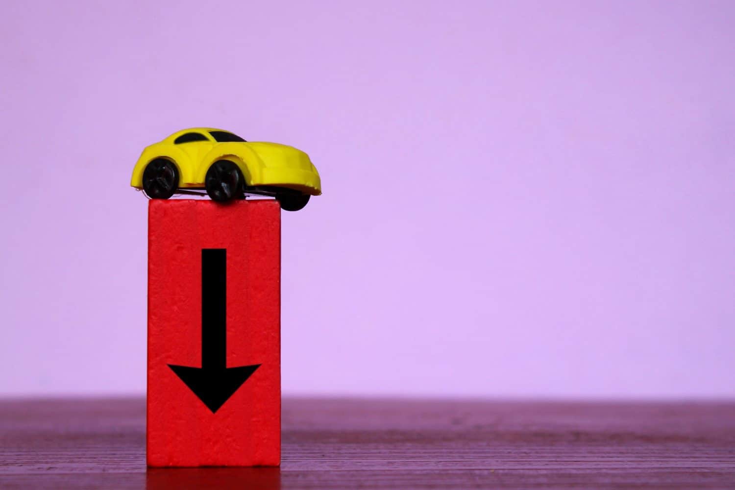 Car depreciation value, price drop concept. Toy car and red wooden cubes with downward arrow.