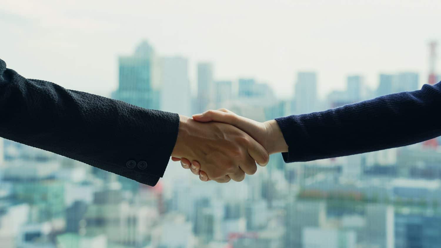 Couple of people shaking hands in front of the city.