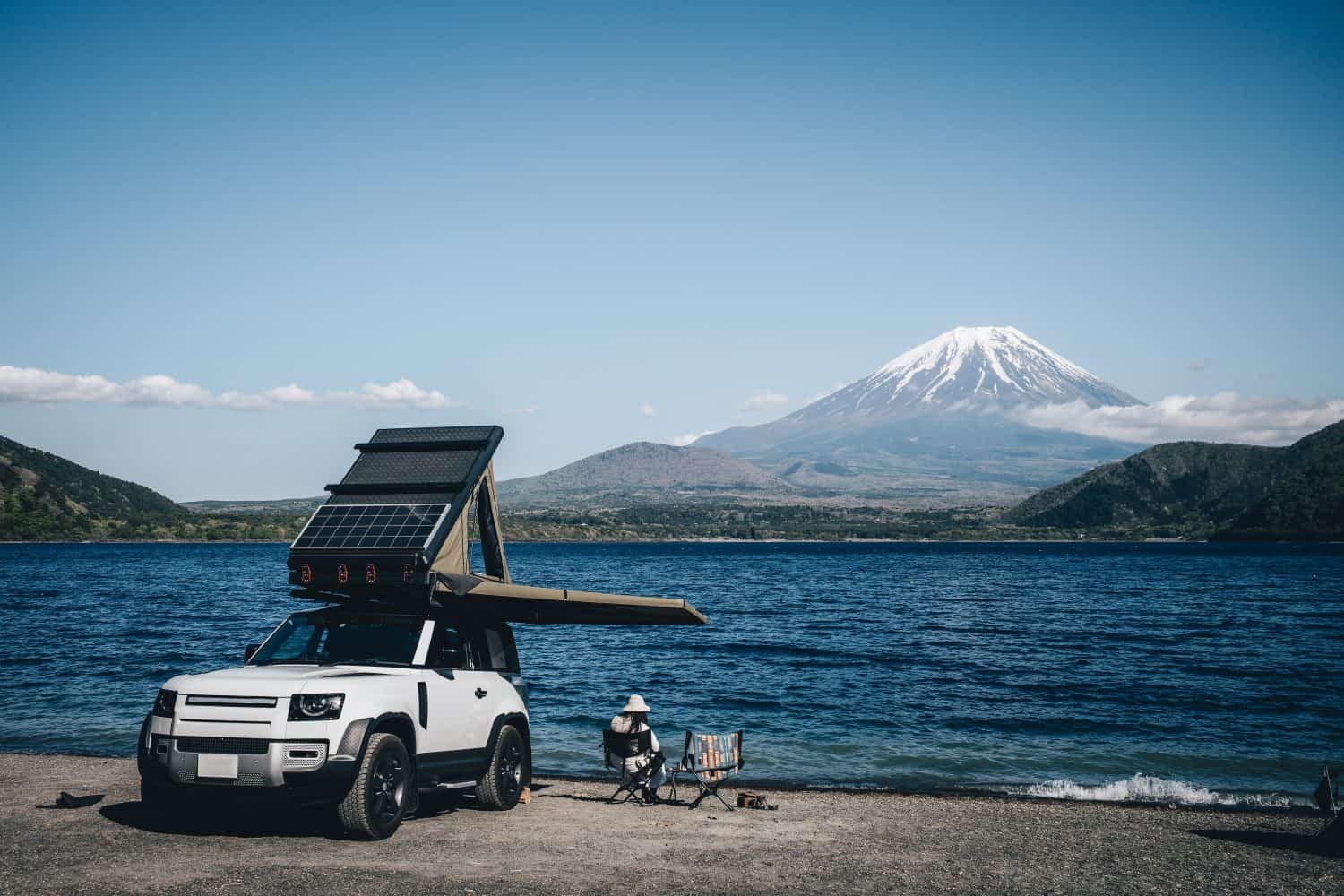 White 4x4 overland car with rooftop tent and awning at the beach and a lake with a view of Mountain Fuji, Japan.